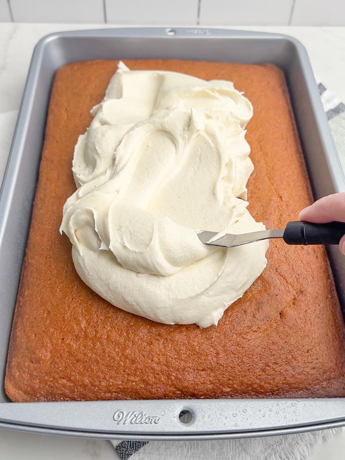 hand holding a spatula spreading cream cheese frosting over pan of pumpkin bars