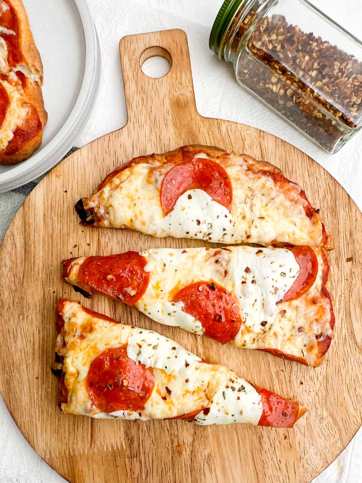 baked pepperoni flatbread cut into slices on a wooden cutting board