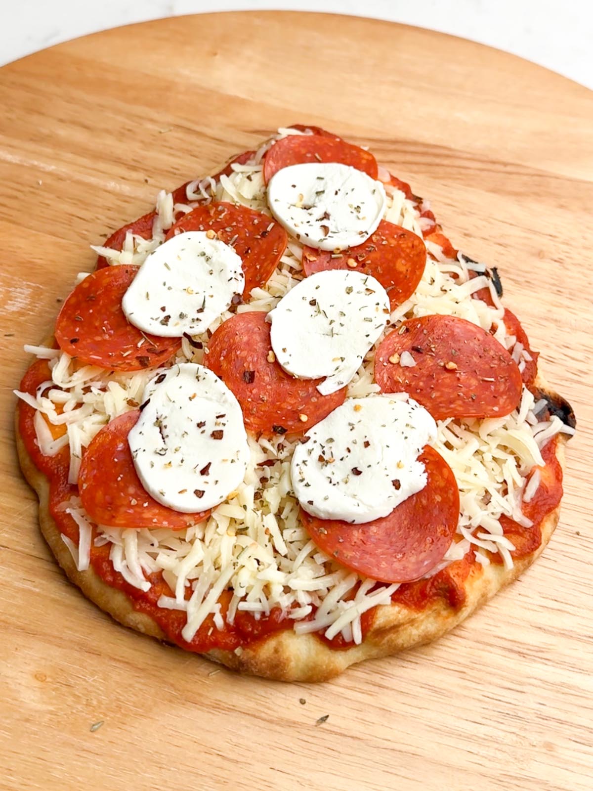 unbaked pepperoni flatbread on a wooden cutting board