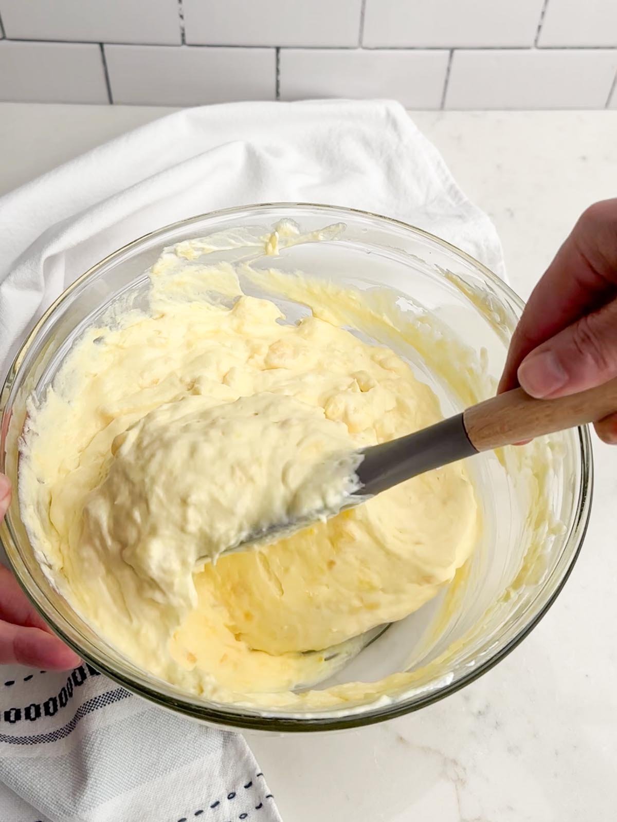 hand holding a spatula folding Cool Whip into the pineapple cream cheese mixture