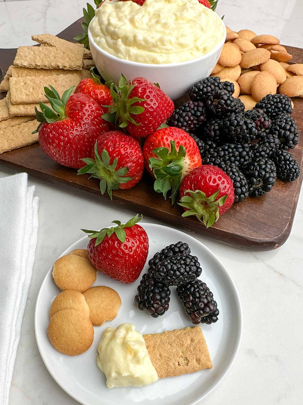 graham cracker with pineapple cream cheese dip on a white plate with fruit and vanilla wafers with fruit plate in background