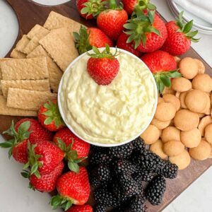 pineapple cream cheese dip in a white bowl on a wooden cutting board with fruit, graham crackers, and cookies