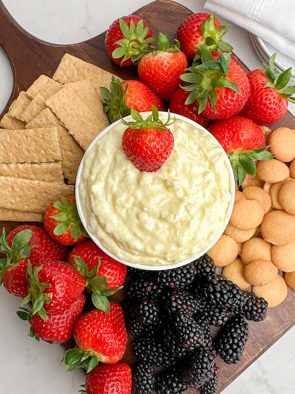 pineapple cream cheese dip in a white bowl on a wooden cutting board with fruit, graham crackers, and cookies