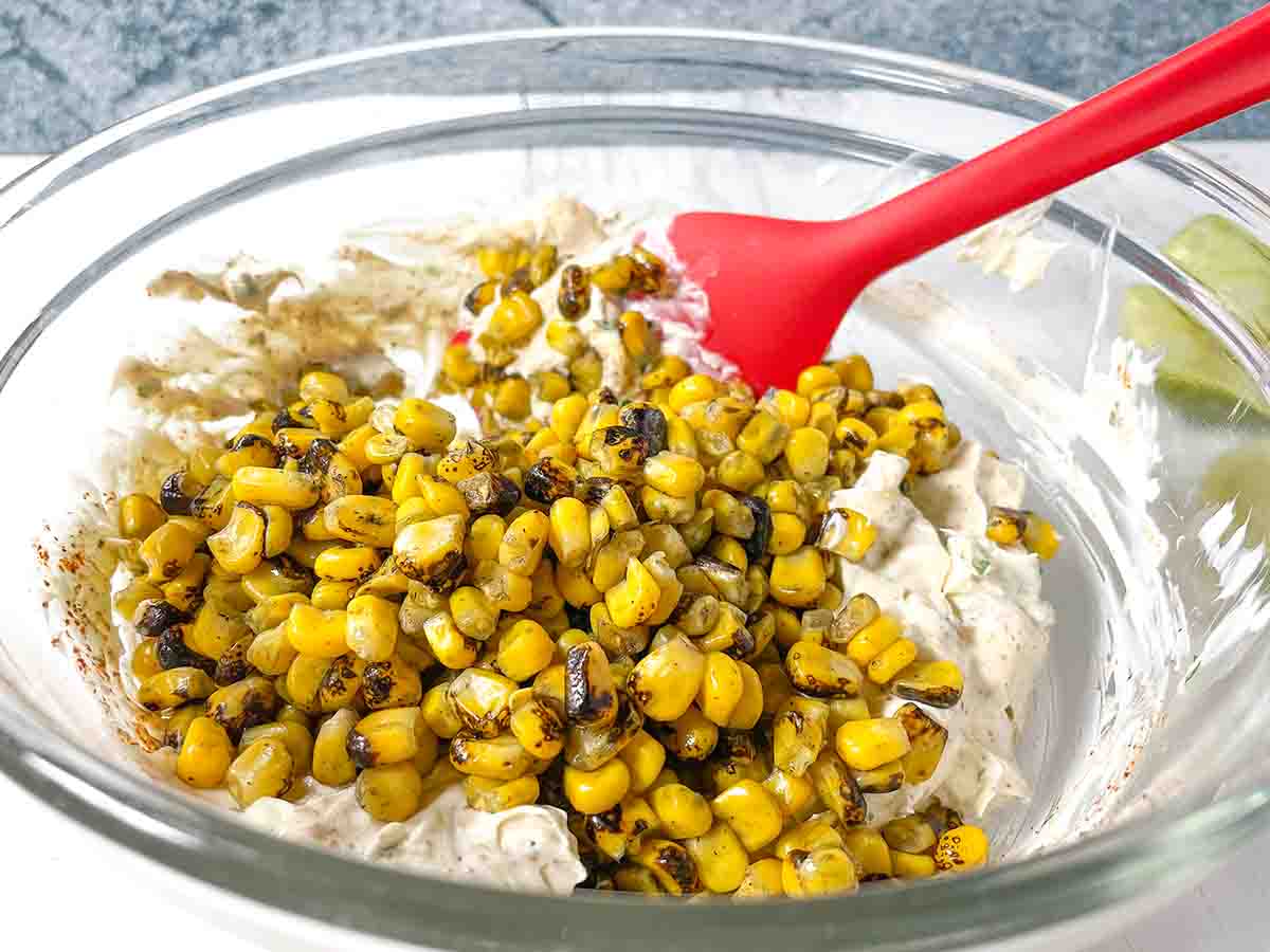 Adding corn to the Mexican Street Corn Pinwheel Appetizer mixture in a clear bowl