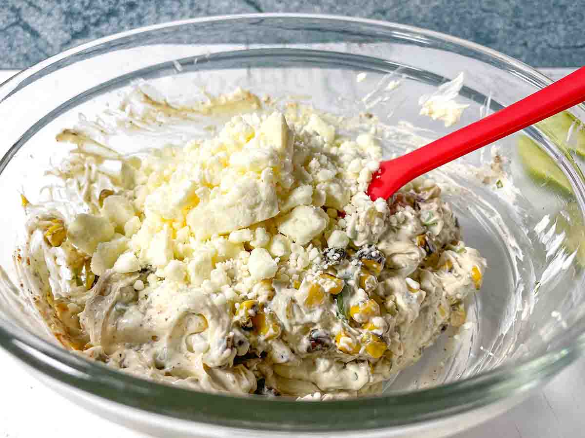 Adding feta cheese to the Mexican Street Corn Pinwheel Appetizer mixture in a clear bowl