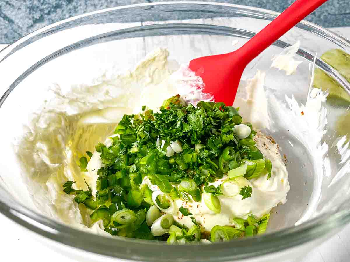 Adding parsley and green onions too the Mexican Street Corn Pinwheel Appetizer mixture in a clear bowl