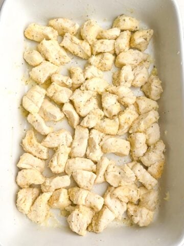 cut up biscuits with seasonings, butter, and cheese in a baking dish.