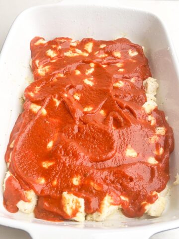 pizza sauce spread over biscuit pieces in a baking dish.