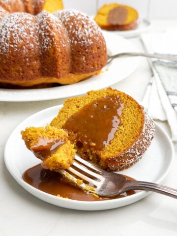 slice of pumpkin cake with yellow cake mix and caramel sauce on a white plate with a fork holding up a bite.
