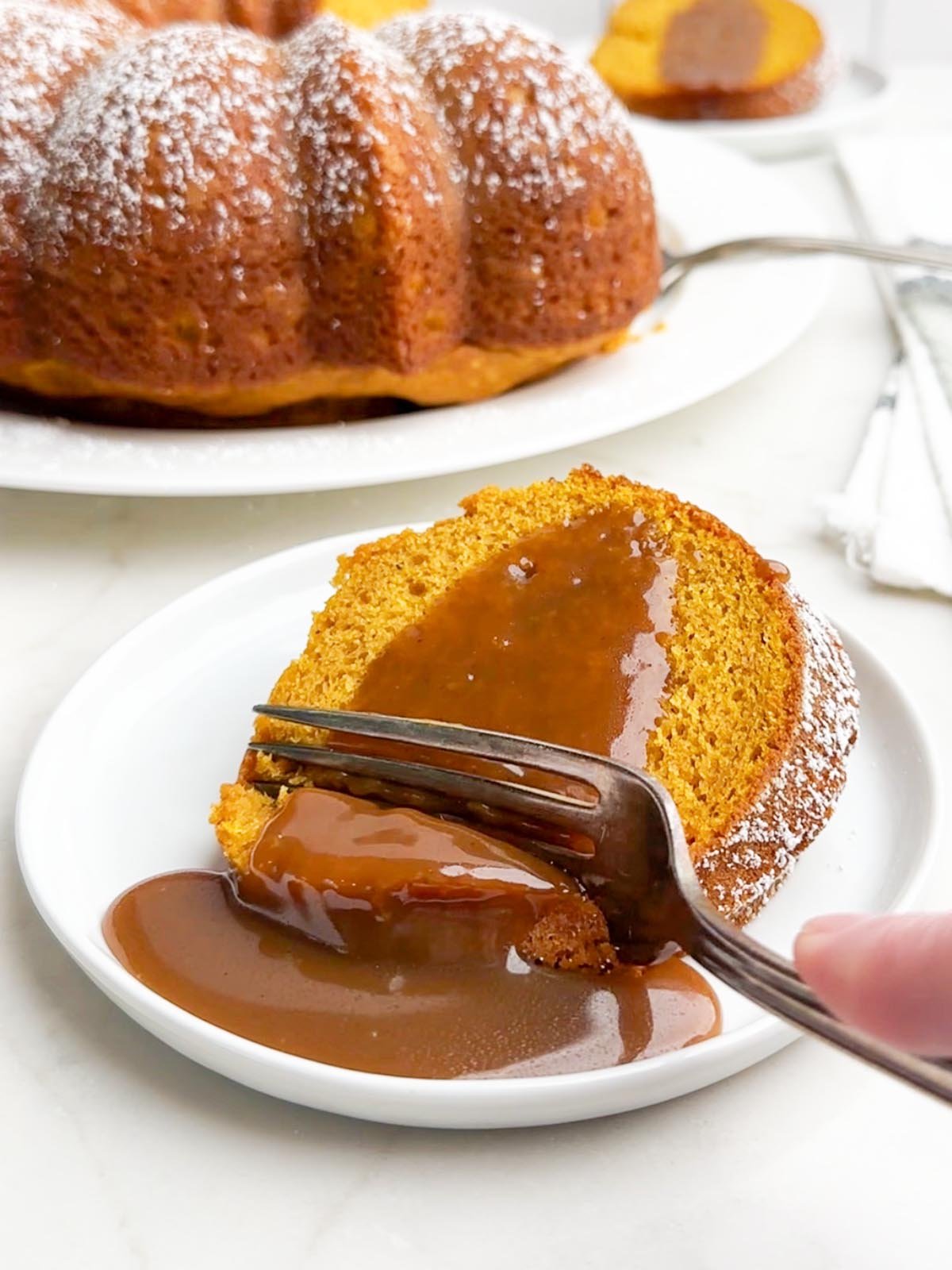fork cutting into a piece of pumpkin cake with yellow cake mix topped with caramel sauce.
