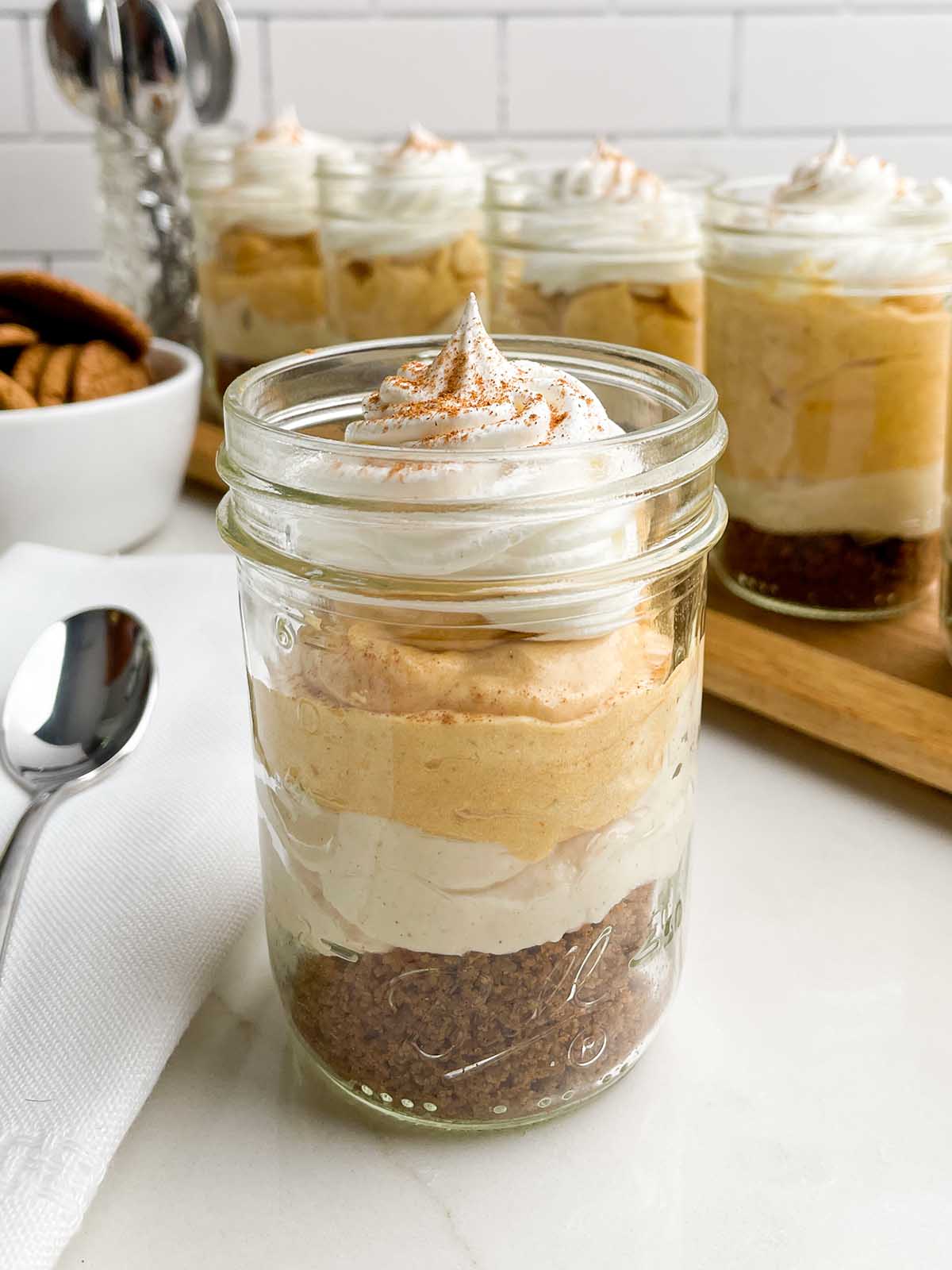a pumpkin pie in a cup with a spoon in front of jars of pumpkin pie in a cup