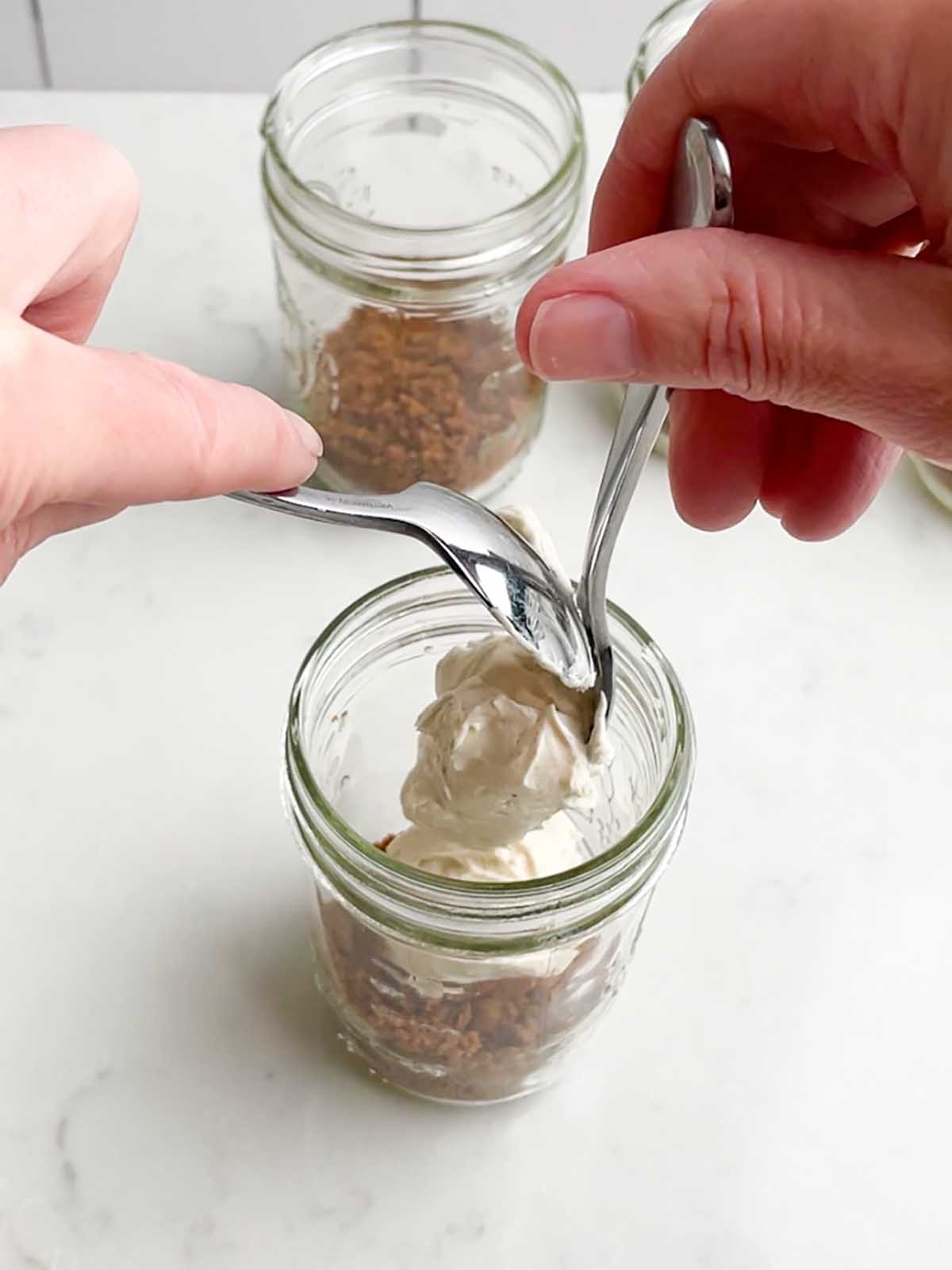 hands holding two spoons dolloping cream cheese mixture into a mason jar