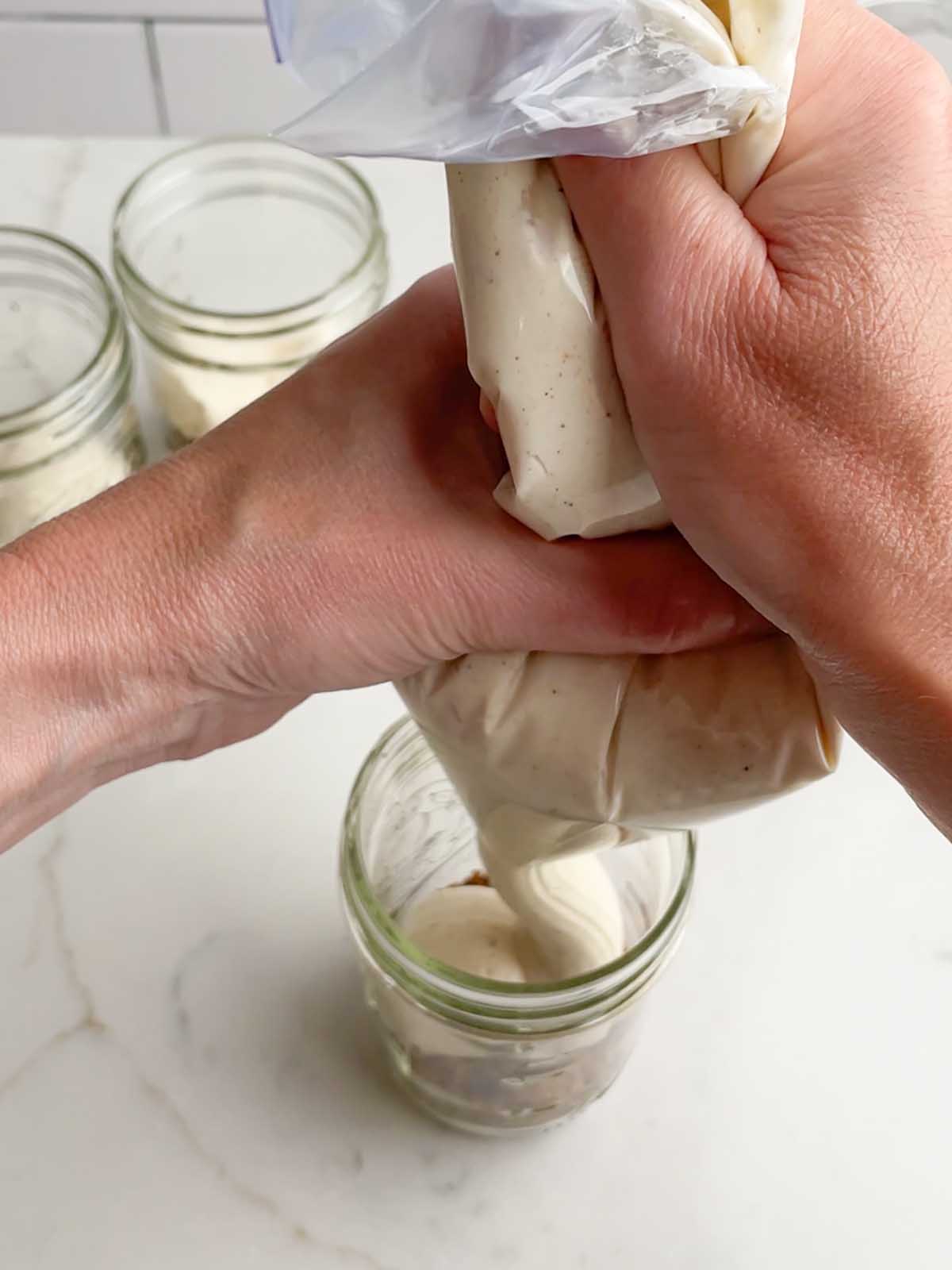 hand holding piping bag squeezing cream cheese mixture into a mason jar