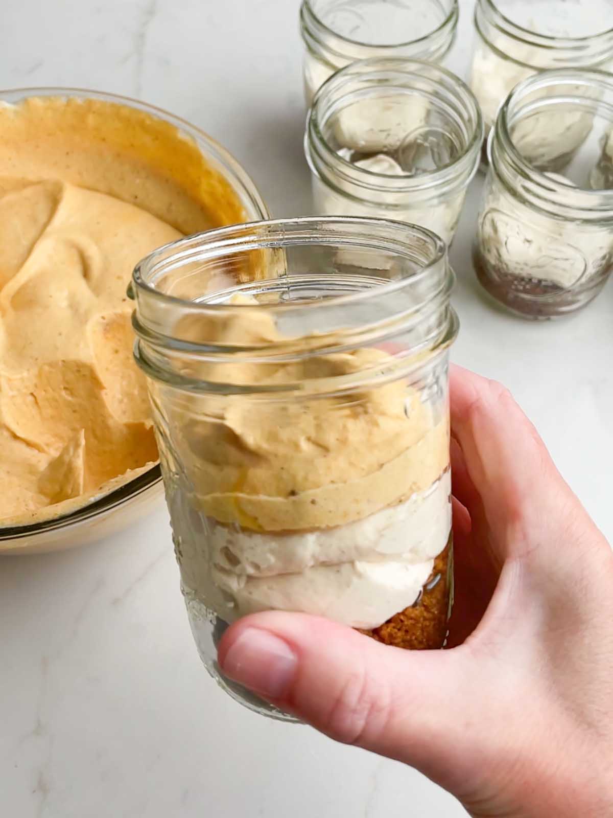 hand holding a mason jar with filled with all three layers of pumpkin pie in a cup