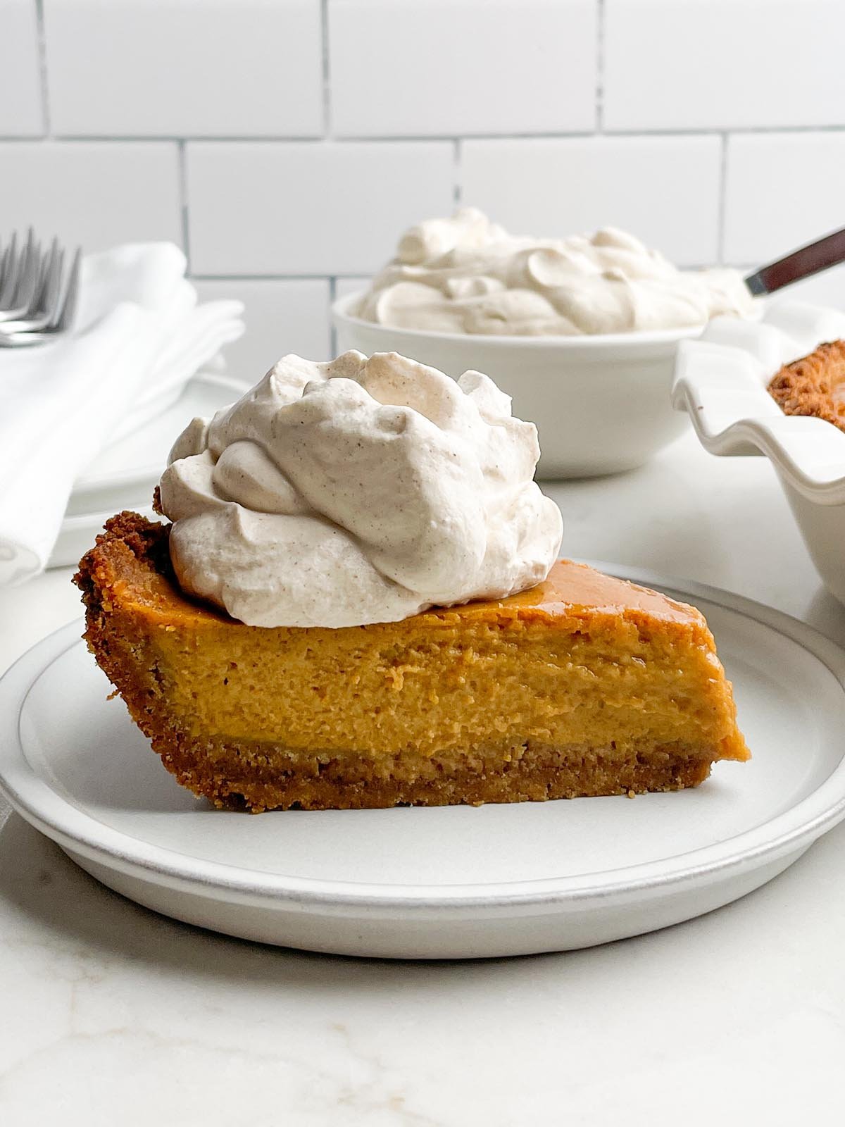 piece of pumpkin pie with graham cracker crust with a dollop of cinnamon brown sugar whipped cream.