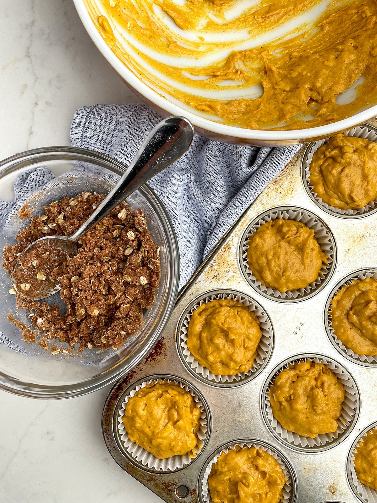 Pumpkin Snickerdoodle Muffin batter in muffin cups with bowl of streusel next to it
