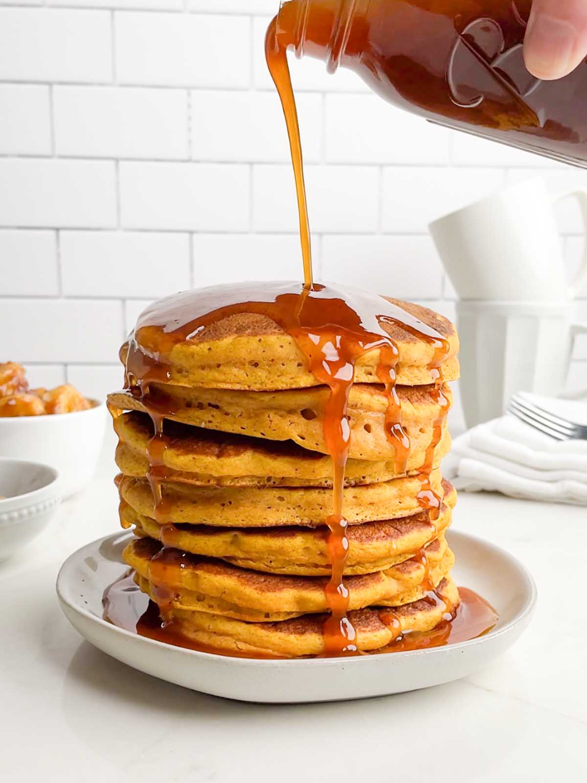 pumpkin syrup being poured onto pumpkin pancakes.