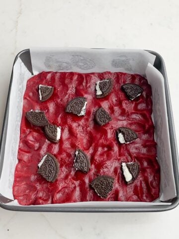 red velvet brownie batter in a square pan with Oreo pieces on top.