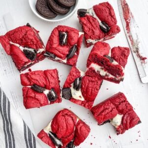 red velvet brownie squares on parchment paper next to a bowl of Oreos, a knife and a black and white napkin