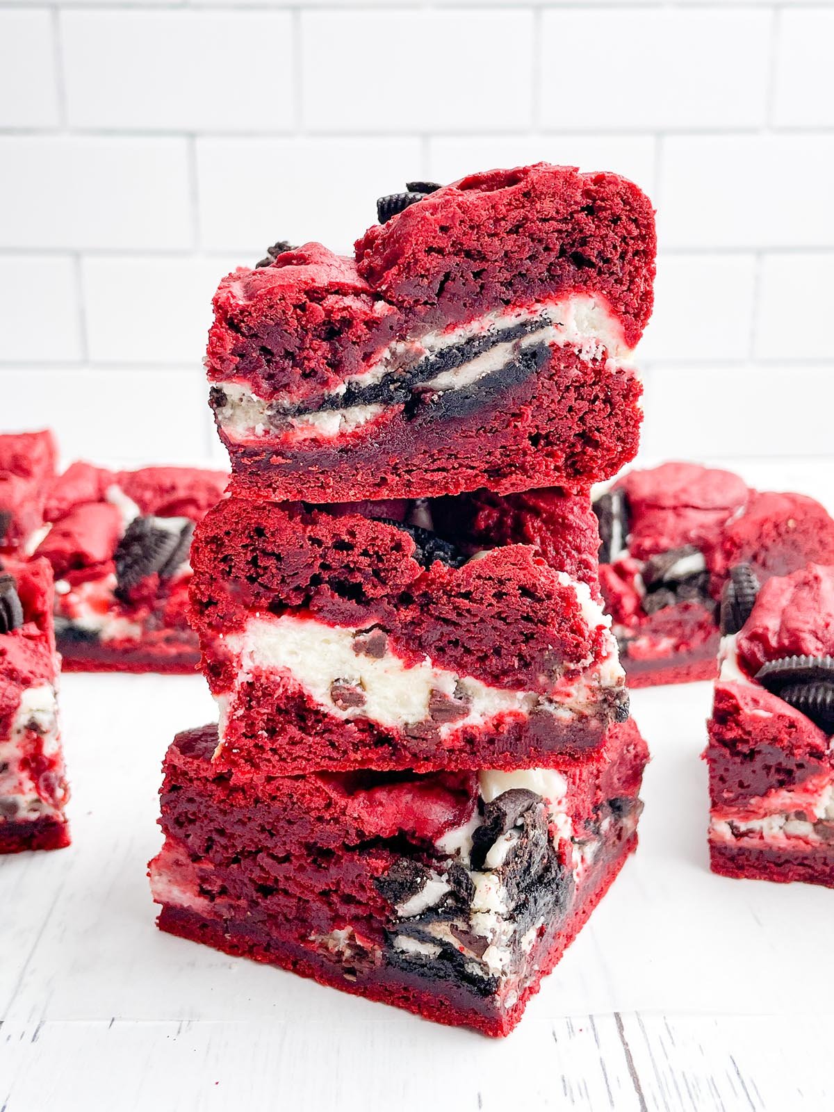 stack of red velvet brownies with red velvet brownie squares in the background.