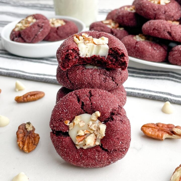 stack of red velvet cake mix cookies with a bite taken out of the top one and plates of cookies in the background