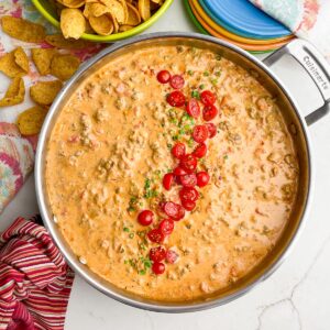 rotel dip in skillet next to plates and a bowl of chips