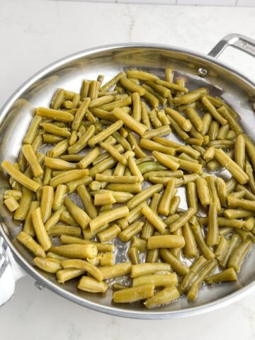 canned green beans in a stainless steel skillet.