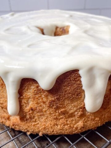 strawberry angel food cake with cream cheese glaze on a wire baking rack.