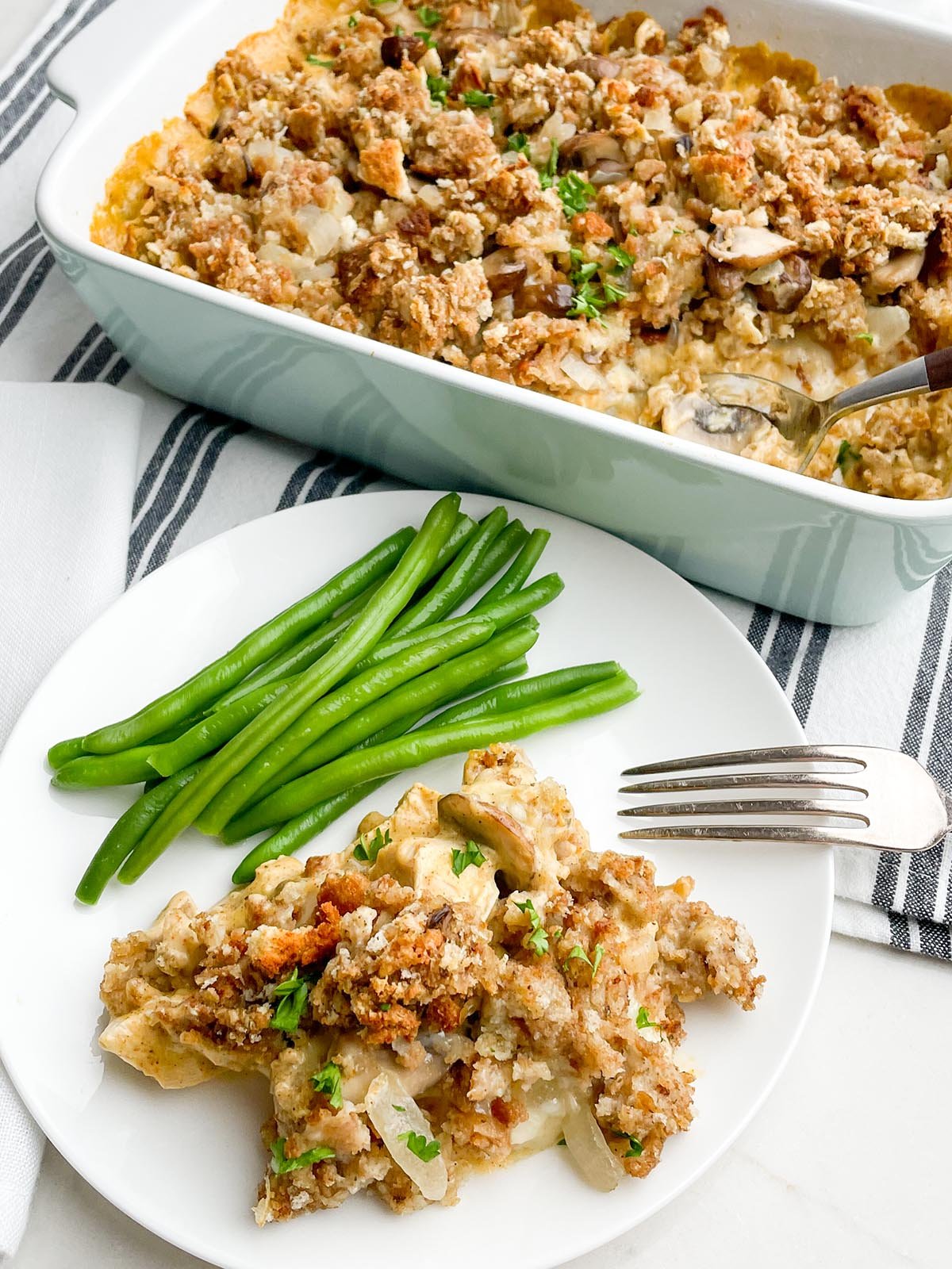 white plate with Swiss chicken casserole and green beans with casserole dish in background
