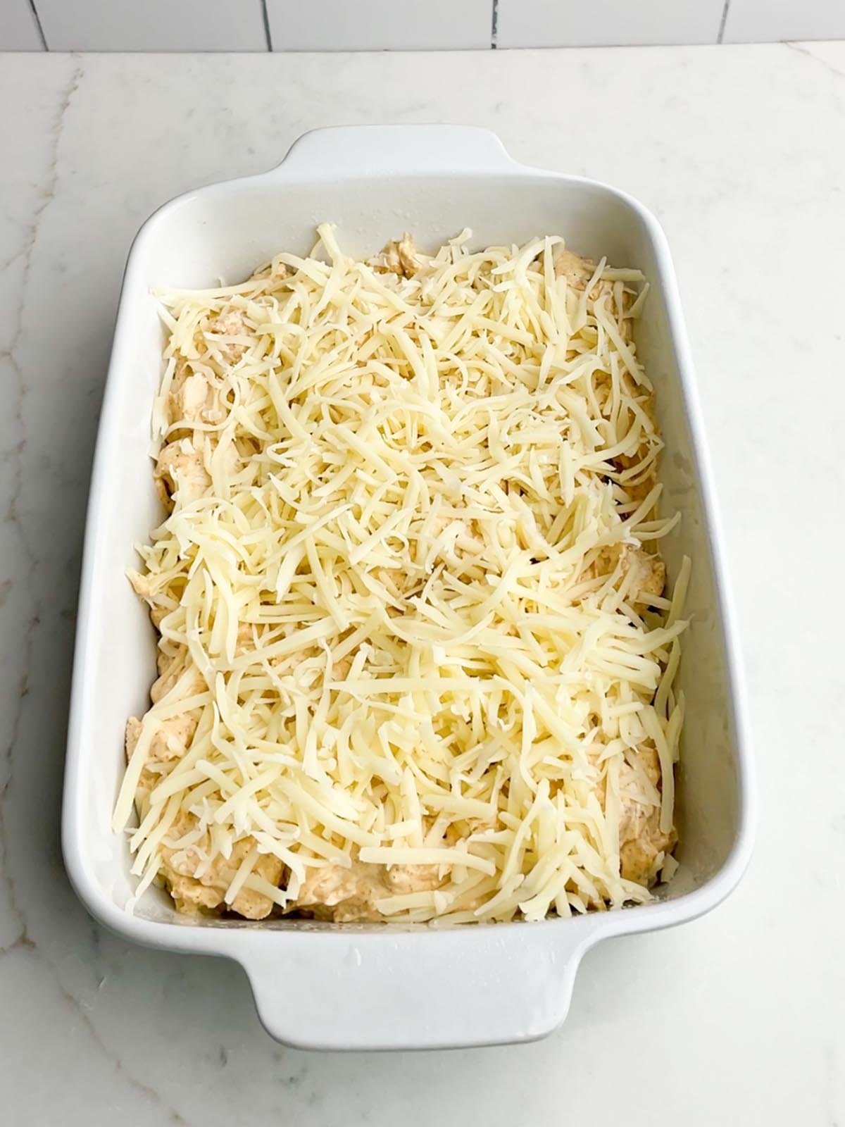 Swiss cheese on top of chicken mixture in white casserole dish