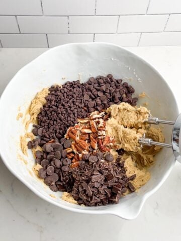 toll house cookie dough with nuts and chocolate chips in white mixing bowl.