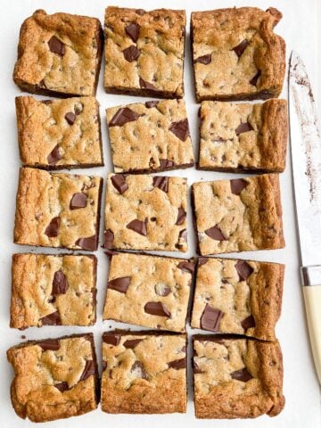 Toll House cookie bars on white parchment paper next to a knife.