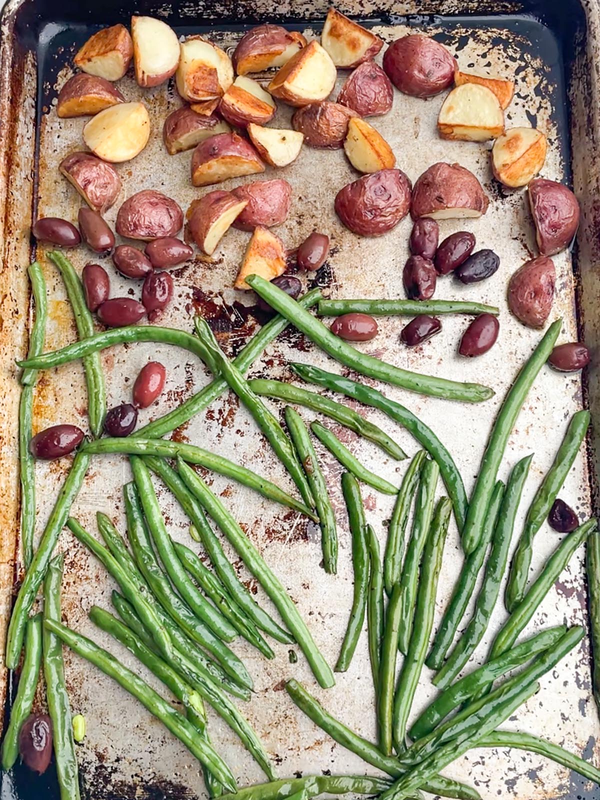 cooked potatoes, olives, and green beans on a sheet pan