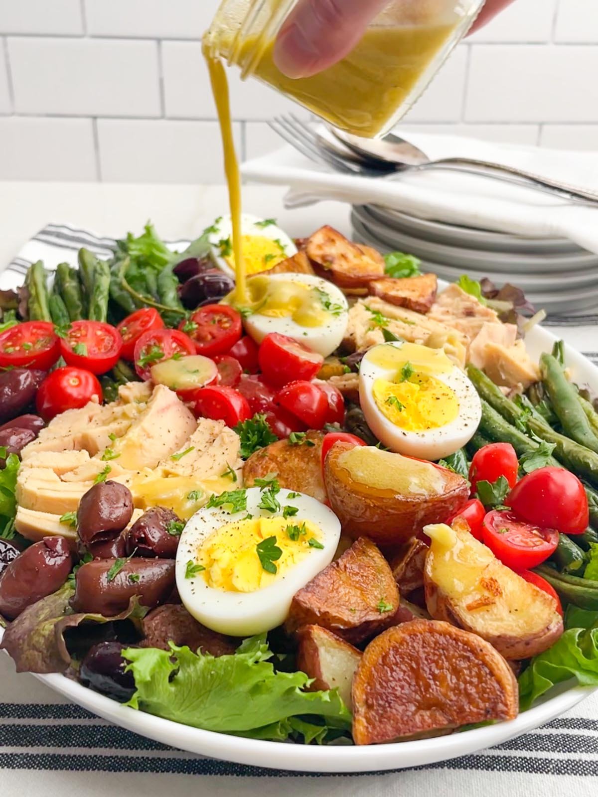 tuna nicoise salad on a platter with dressing being poured on top