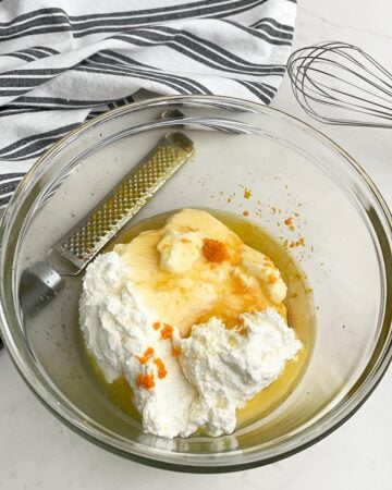 clear bowl with ricotta, orange juice and zest, and honey next to a microplane.
