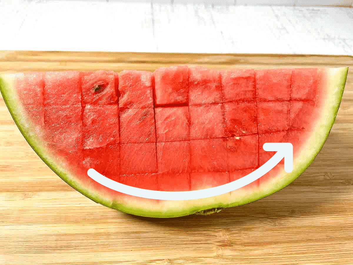 Watermelon quarter on a wooden cutting board with a while arrow running along the curved rind